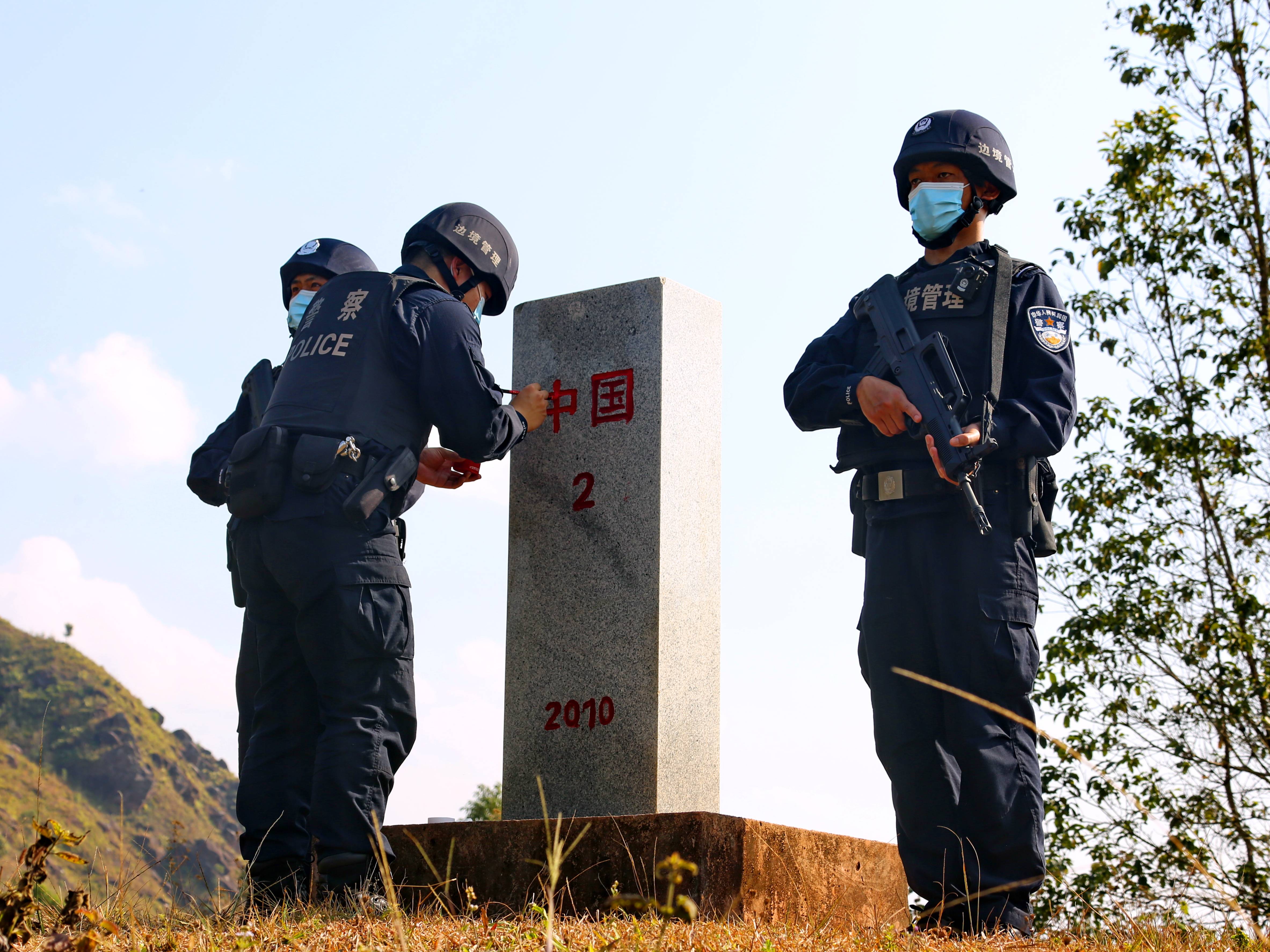 图为普洱边境管理支队移民管理警察用红色油漆为界碑描红