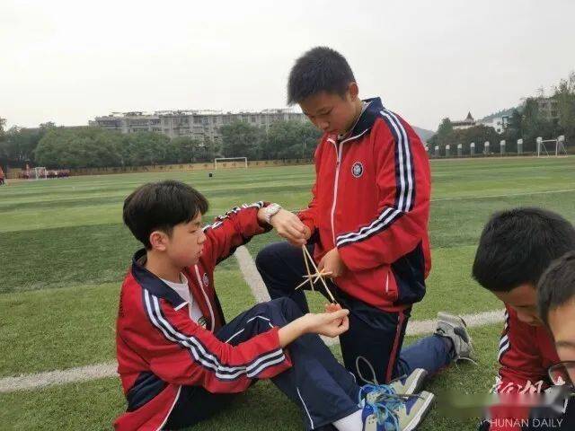 八年级学生按班级组小队在运动场一字排开,开始了"筷子搭桥"比赛活动