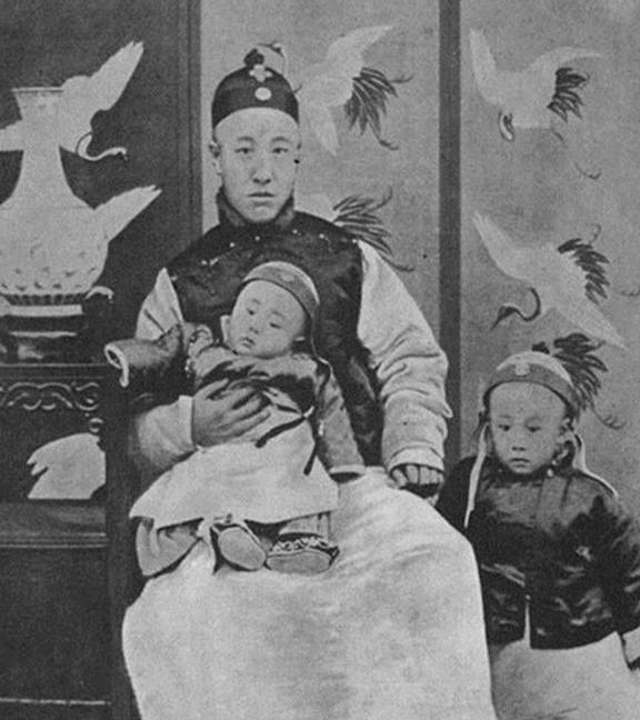 载沣抱着的萌娃是末代皇帝溥仪的弟弟溥杰,年幼的溥仪则乖巧站在一旁.