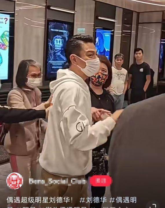 刘德华身穿白色连帽卫衣,棕色短裤和运动鞋.