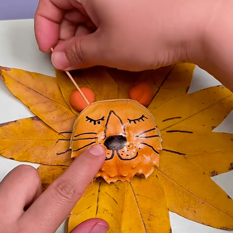 取少量橙色黏土,搓成圆形后粘贴至蟹壳上方,作为狮子的耳朵·将洗净